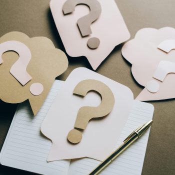 Artistic paper question marks on an open notebook with a pen, symbolizing curiosity and creativity.
